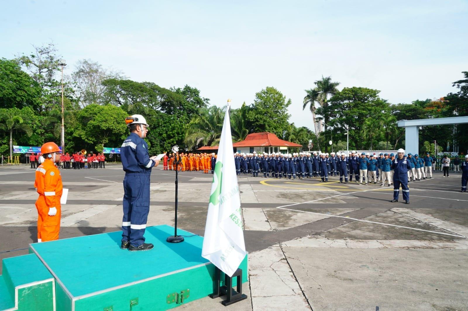 Pembina apel ber-coverall dan berhelm memimpin apel Bulan K3 di depan barisan pekerja ber-APD
